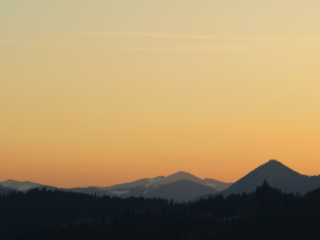 Morning landscape with mountains and orange sky at sunrise with sun reflecting. Evening sunset on the horizon of hills with snow and sun rays.の写真素材