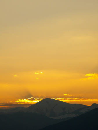 Morning landscape with mountains and orange sky at sunrise with sun reflecting. Evening sunset on the horizon of hills with snow and sun rays.の写真素材