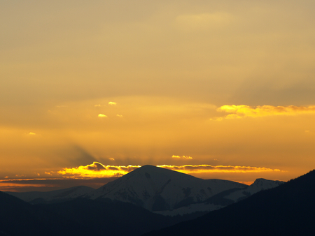 Morning landscape with mountains and orange sky at sunrise with sun reflecting. Evening sunset on the horizon of hills with snow and sun rays.の写真素材