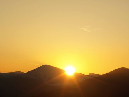 Morning landscape with mountains and orange sky at sunrise with sun reflecting. Evening sunset on the horizon of hills with sun rays.の写真素材