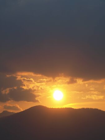 Morning landscape with mountains and orange sky at sunrise with sun reflecting. Evening sunset on the horizon of hills with snow and sun rays.の写真素材