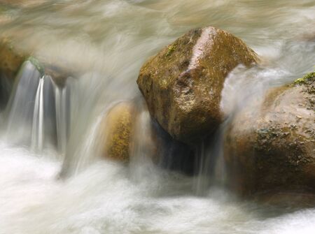 Small waterfall in the mountain river. Beautiful natural background of stones and with flowing, blurring water and foaming.の写真素材