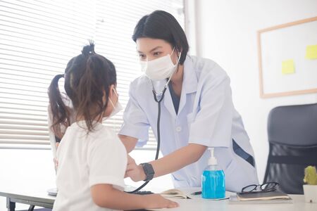 An Asian female doctor wearing a surgical mask is checking the child patient's heart rate with a stethoscope.の写真素材