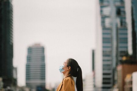 An Asian woman stood in the metropolis and closed her eyes and breathed through a face mask.