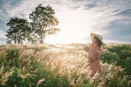 An Asian girl on a beautiful spring meadow at sunset. She wears a pink dress and wide-brimmed hat. This photo was taken using a vintage concept.の写真素材
