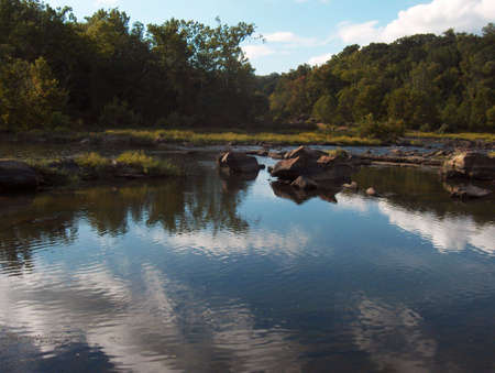 A river flows between rocks under a clear, blue sky with trees on the shorelineの写真素材