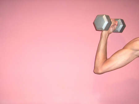 Woman flexes bicep with dumbbell against pinkの写真素材