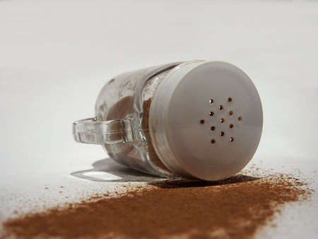 Cinnamon spilled from glass shaker lying on side on white backgroundの写真素材