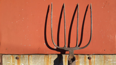 Old garden tool. dirty rusty pitchfork on red metal surface with shabby paint. close-up objectの写真素材