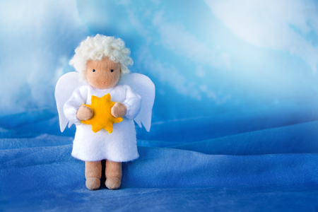 White felt Christmas angel with yellow star in hands on blue silk background, toned.の写真素材