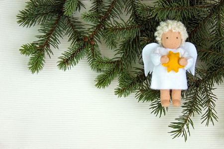 White felt Christmas angel with yellow star in hands to fresh natural branches of Christmas tree spruce on textile background. Top view. Flat layの写真素材