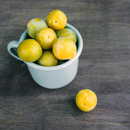 Fresh yellow plums in enameled cup on wooden rustic background. Russian homemade fruit. Top view.の写真素材
