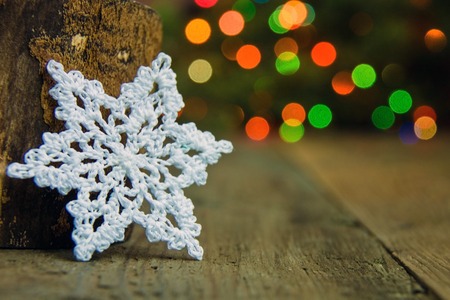 White cotton crocheted snowflakes near green fur tree on the rustic wooden background. Christmas vivid concept. Red, blue, yellow and green spots of blur de focused glittering lights. Bokeh. Rusticの写真素材