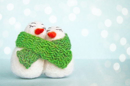 Family of white happy loving felted wool snowmen with green knitted scarf on bright blue background....