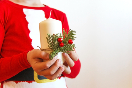 Child dressed in red Christmas pajamas holding in hands a white candle decorated with a branch of spruce tree and berriesの写真素材