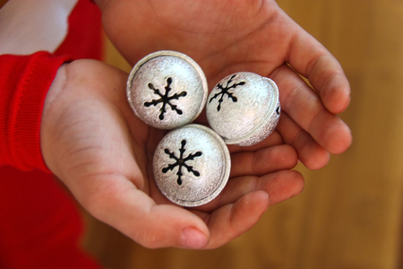 Child dressed in red Christmas pajamas holding in hands silver bells with snowflakesの写真素材