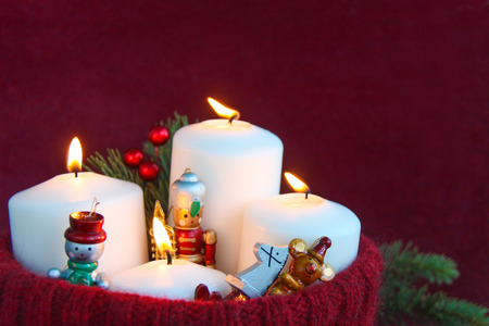 Four white Christmas advent candles with a burning flame and rustic wooden toys in a handmade knitted red wool hat with fir branches against a burgundy velvet paper. Red pear or jester red colorsの写真素材