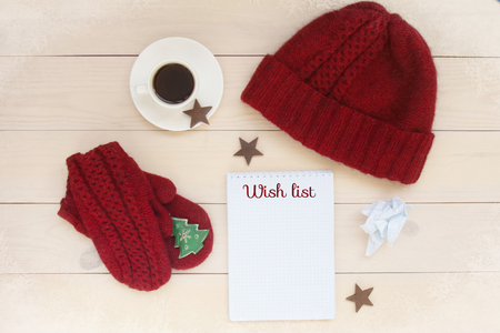 Christmas decoration background with red handmade knitted hat,mittens, toy spruce fir, cup of coffee,wooden stars, blank list for holiday wish.の写真素材