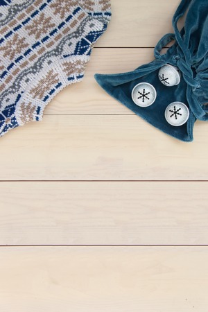 Christmas decoration wooden background with knitted wool sweater with jacquard ornament, blue velvet bag with bells snowflakes.の写真素材