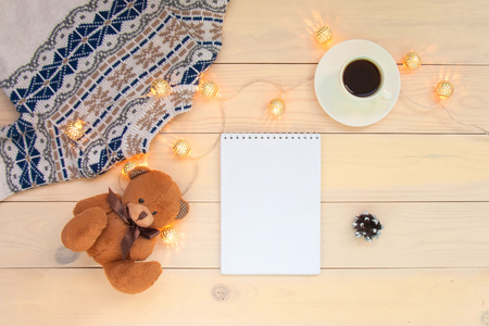 Christmas decoration wooden background with knitted wool sweater with jacquard ornament, brown bear toy, cup of coffee., christmas lights, check list.の写真素材