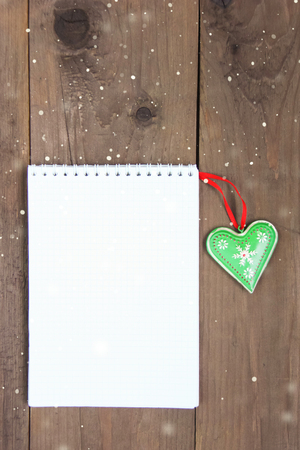 Christmas decoration wooden background with blank list for holiday goals, beautiful green heart with ornament. snowflakes. Closeup. Flatlayの写真素材