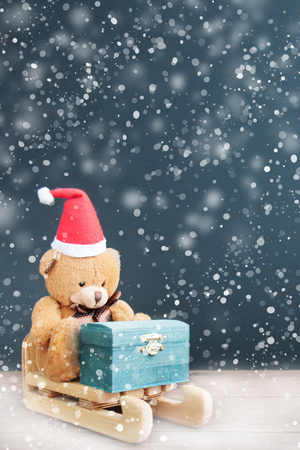 Decoration Santa's helper bear in a red hat rides a sleigh with a chest of gifts in the snowfall at Christmas. Front view, close up. Snowflake. Holiday greeting card concept. Copy spaceの写真素材