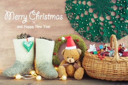 Santa's helper bear in a red hat boots with pine cones toys with a Christmas tree crocheted napkin with beads garland a wreath of moss with red berries on a wooden background.Xmas card conceptの写真素材