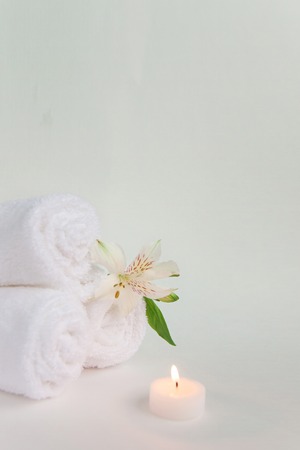 Beautiful alstroemeria flower, burning candle and three rolls of clean white spa salon bath towels isolated on white background. Front view copy space close upの写真素材