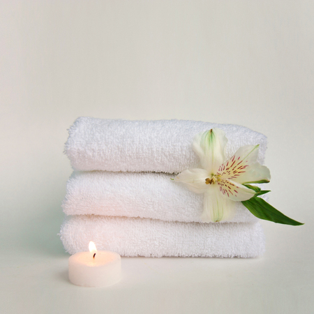 Beautiful alstroemeria flower, burning candle and stack of three clean white spa salon bath towels isolated on white background. Front view copy space close upの写真素材