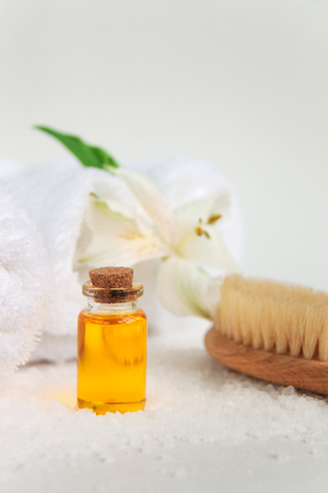 Beautiful alstroemeria flower, bottle with cosmetic oil, wooden brush, three rolls of clean white spa salon bath towels isolated on white background. Front view close upの写真素材