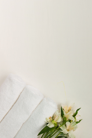 Beautiful alstroemeria flower and three rolls of clean white spa salon bath towels isolated on white background. Top view flat lay copy space closeupの写真素材