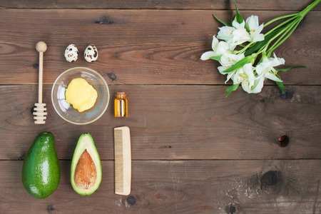Ingredients for vitamin avocado skin care facial mask green lime, bottle cosmetic oil,honey,dipper, oat-flakes, hair brush on brown wooden background.の写真素材