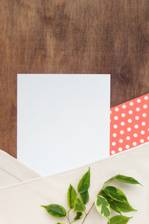 Beautiful background of paper of color living coral polka dot and white with a beige plaid and green branch of ficus benjaminon a wooden background with copy space for text.Top view, close up flatlay.の写真素材