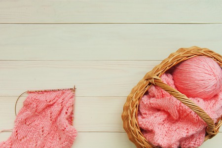The process of knitting coral karigan with an openwork pattern on wooden knitting needles and a basket on the background of a table of light wooden boards. Top view flatlay copy space for textの写真素材