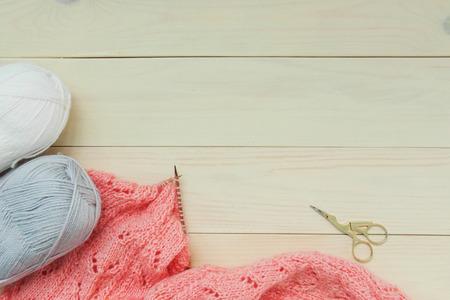 Knitting process of coral cardigan made of wool on wooden knitting needles with gray and white yarn...