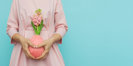 Magnificent blooming hyacinth in a ball of wool yarn color living coral in the shape of easter egg in the hands of a young woman dressed in pink dressl. Front view, web banner, copy space for textの写真素材