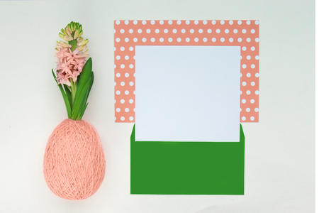 Magnificent blooming hyacinth in a ball of coral pink wool yarn in the shape of easter egg, paper coral and white polka dot with green envelope with copy space for text. Top view, close upの写真素材