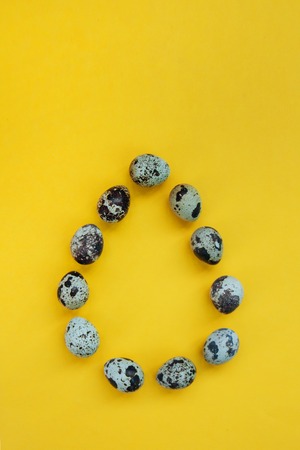 Colorful composition of Easter quail eggs on pastel yellow background with copy space for text. Card concept, symbol of new life. Flat lay, close up, top view, vertical.の写真素材