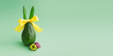 Beautiful creative decoration background idea with fresh green avocado rabbit yellow ribbon bow, quail eggs on matte paper.Vibrant food spring card concept. Closeup.Front view. Copy space. Web bannerの写真素材
