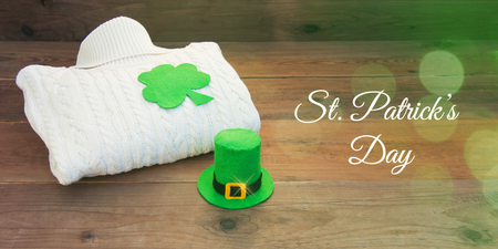 White irish aran pattern knitted wool sweater pullover with decoration for Saint Patrick's Day on the rustic wooden background. Felt clover trefoil green leaf, leprechaun hat. Front view, web bannerの写真素材