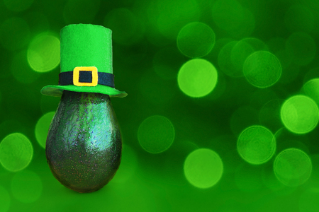 St. Patrick's day decoration background idea with fresh green avocado in leprechaun hat on bright bokeh glittery background. Card concept. Closeup. Front view. Copy spaceの写真素材