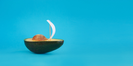 Beautiful creative decoration background idea with fresh green avocado yacht, sailboat with white sail on blue paper sea. Closeup. Front view. Copy space,banner. Food, freedom and adventure conceptの写真素材