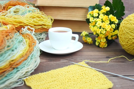 Knitting of yellow, blue wool with needles, white espresso coffee cup saucer, old books, Kalanchoe on wooden rustic background. Front viewの写真素材