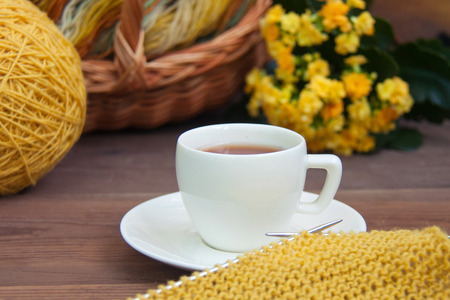 Knitting of yellow wool with needles, white espresso coffee cup saucer, basket, Kalanchoe on wooden rustic background. Front viewの写真素材