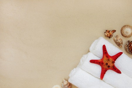 Red starfish and mollusk shells on pure white fine beach sand. Three rolls of clean white spa salon bath towels.Sea relax background with place for text, copy space. Top view, copy spaceの写真素材