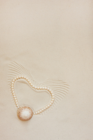 Heart-shaped pearl necklace on white fine sand with sea shell. Front view, copy space for text, flat layの写真素材