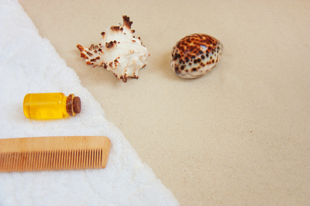 Beautiful spa set with clean white bath towel on a sandy background. Sea shells, oil bottle, hair brush. Front view, copy space.の写真素材