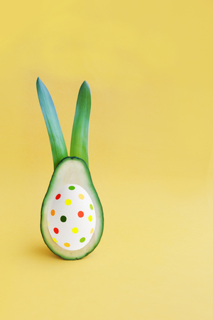 Decoration Easter holiday background with fresh green half avocado rabbit and bones like an painted egg on bright paper. Minimal healthy food card concept. Closeup. Front view. Copy space.の写真素材