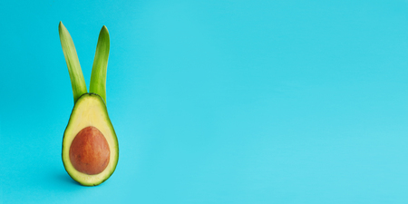Decoration Easter holiday background with fresh green half avocado rabbit and bones like an painted egg on bright paper. Minimal healthy food card concept. Closeup. Front view. Copy space. Web bannerの写真素材