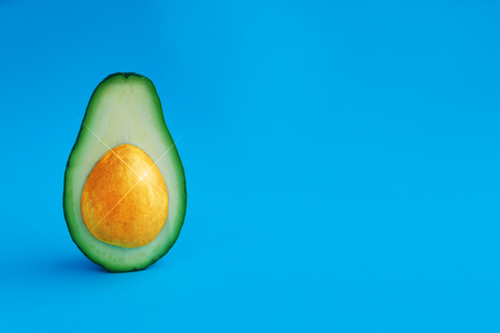 Decoration Easter holiday background half avocado with golden bones with sparkle like an painted egg on bright blue paper. Minimal healthy food card concept. Closeup. Front view. Copy space.の写真素材